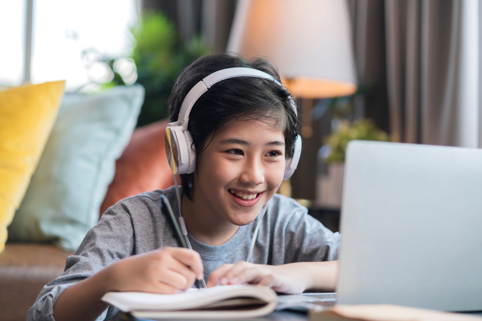 Asaian child Boy kid  taking an E-learning learning online class from school teacher by digital remote device laptop internet meeting in living room ,asia teen wear headphone using laptop e learning class at home